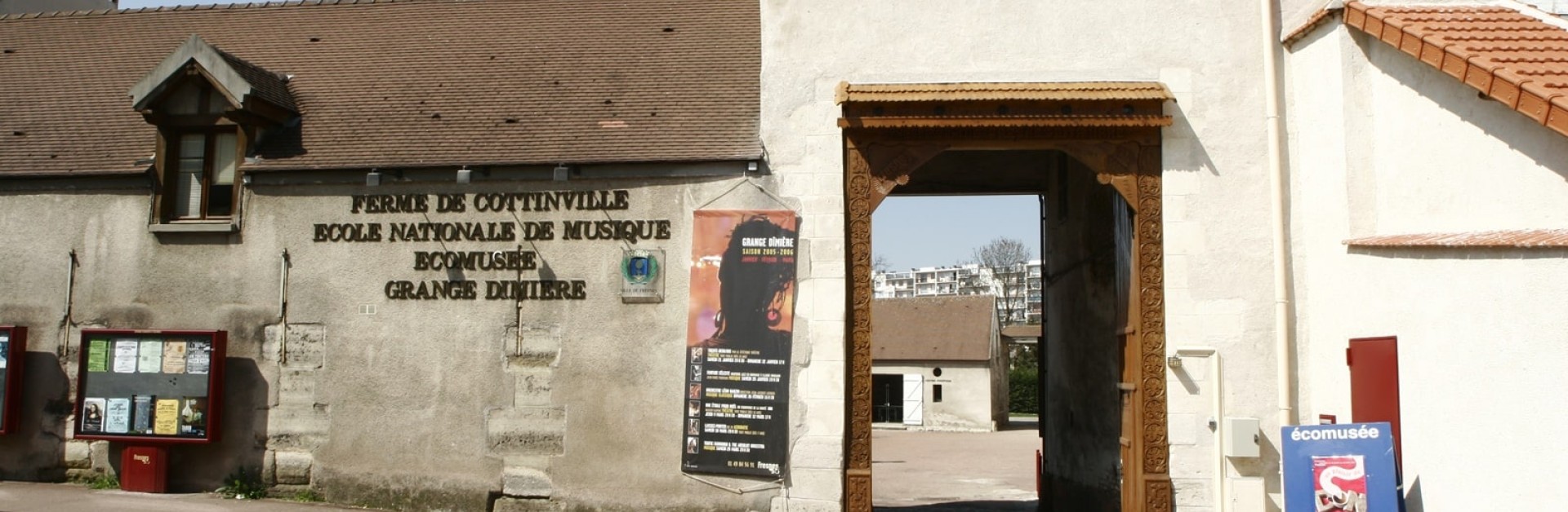 Entrée d'une ancienne ferme qui laisse apercevoir une cour et des immeubles en fond.