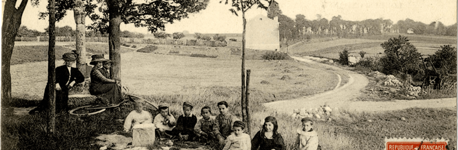 Femmes et enfants assis dans l'herbe au calvaire de la route de Montjean de Fresnes