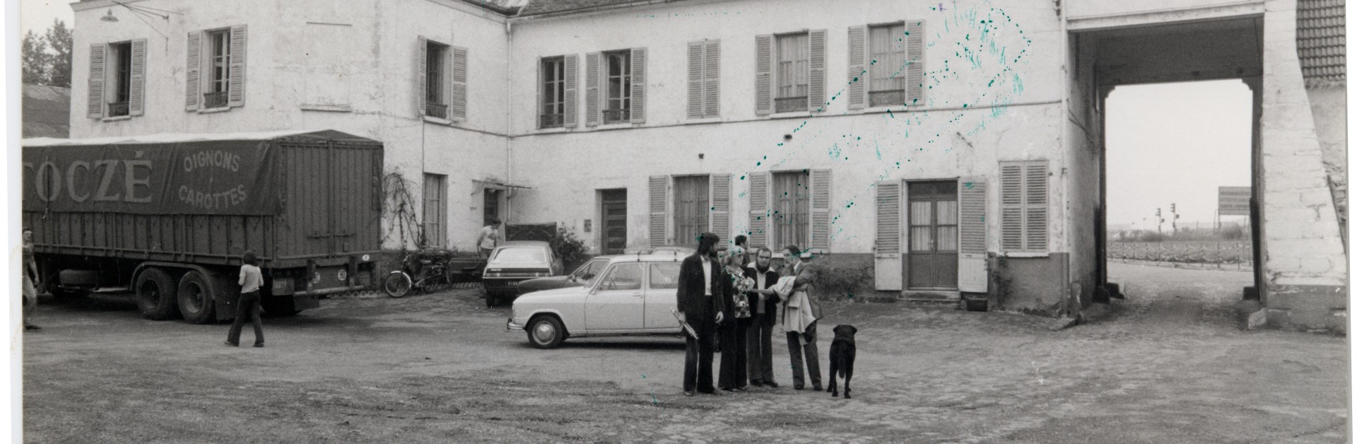 Carte postale en noir et blanc montrant un groupe de personnes se tenant au milieu de la ferme