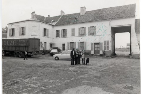 Carte postale en noir et blanc montrant un groupe de personnes se tenant au milieu de la ferme