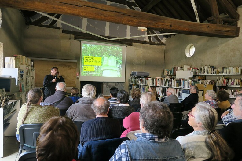 Dans une ancienne grange réhabilitée, un conférencier présente sur écran devant une salle pleine de personnes majoritairement âgées - Agrandir l'image, fenêtre modale
