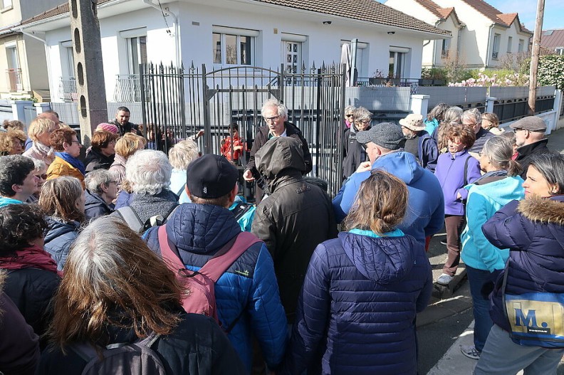 Un conférencier à un angle d'une rue face à de nombreux spectateurs, de dos sur la photo - Agrandir l'image, fenêtre modale